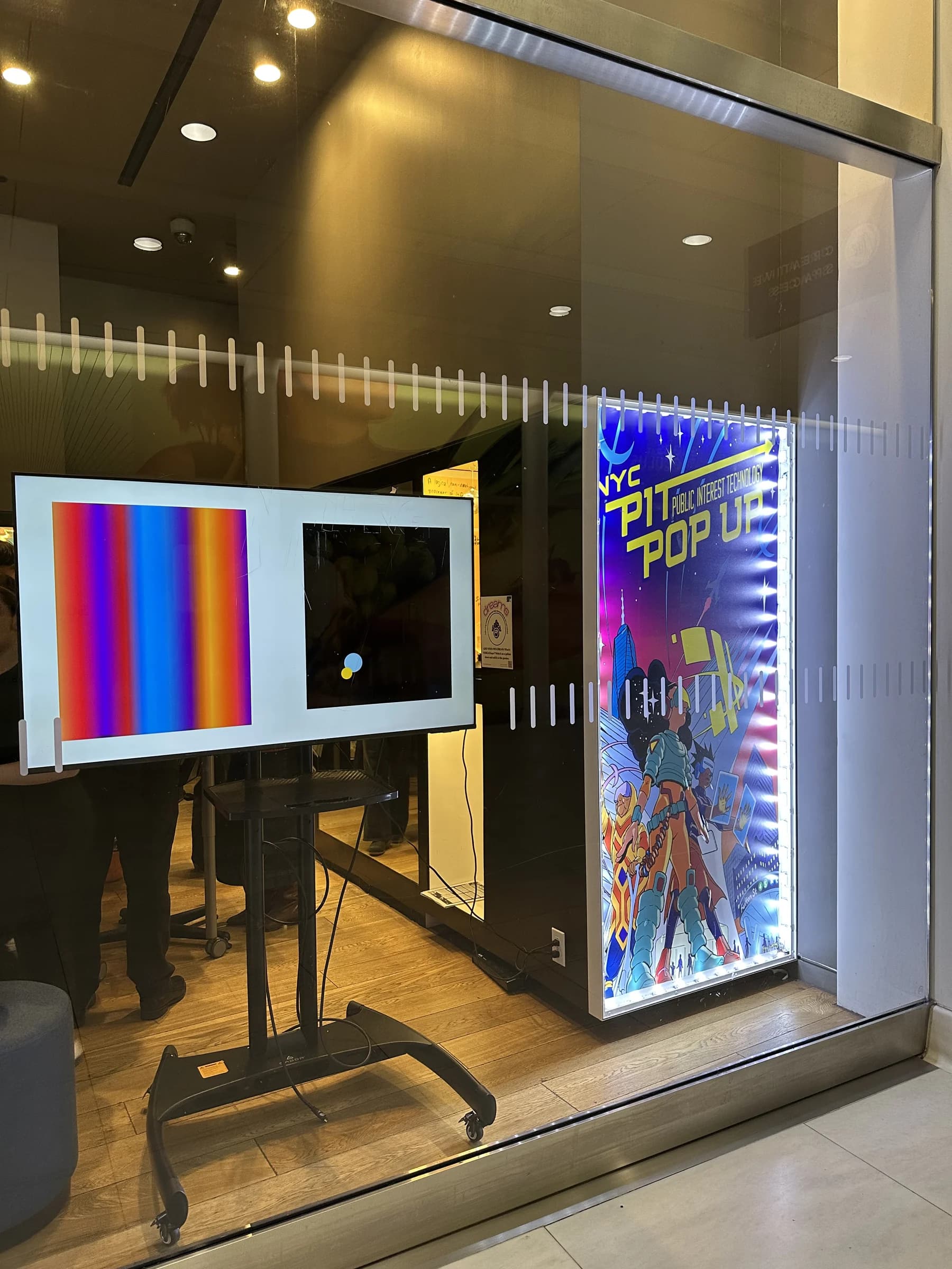 The installation seen through a window beside an illuminated NYC Public Interest Technology Pop Up sign.