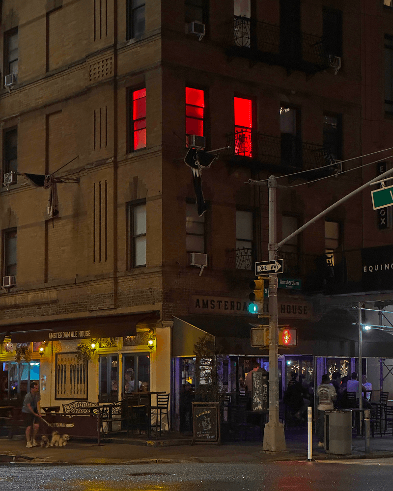 Three studio windows glowing red above a New York street at night.